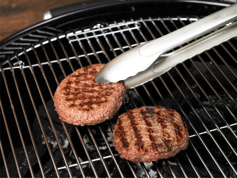 Rösle Grillzange mit persönlicher Gravur wendet eine Frikadelle auf dem Grill.