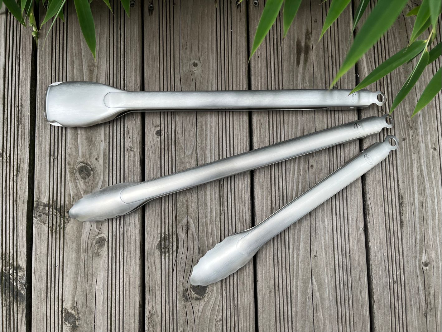 Drei Edelstahl Grillzangen auf einem Hozdeck